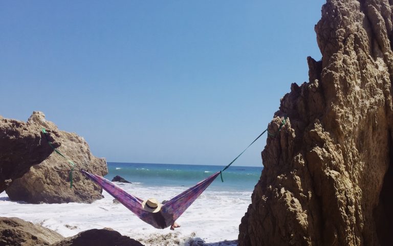 girl in a hammock between rocks on a beach